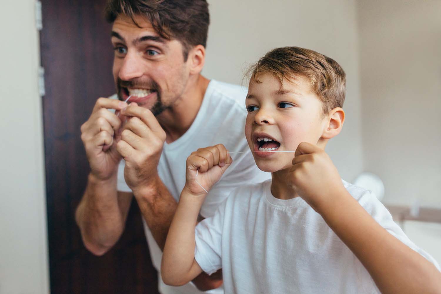 A father and son, patients at West Richland Family dental, floss together during their daily home oral care routine.
